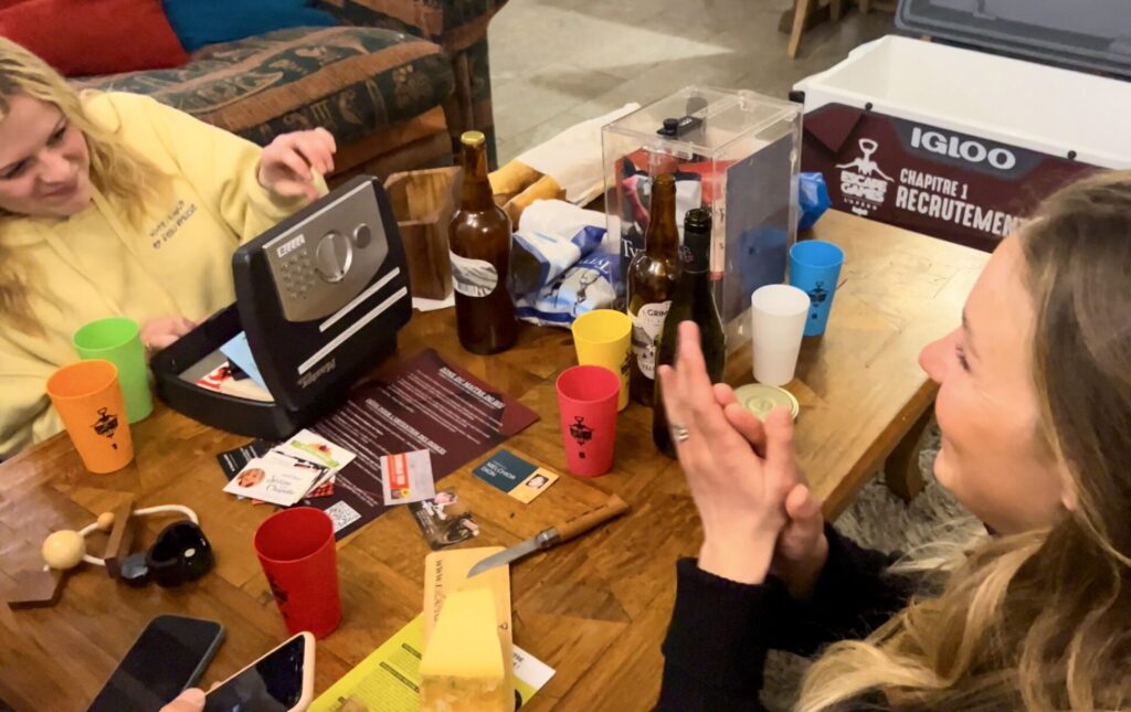 Deux personnes qui jouent à l'EGA. Sur une table il y a des verres colorés, une boîte à code et des aliments d'apéritif.